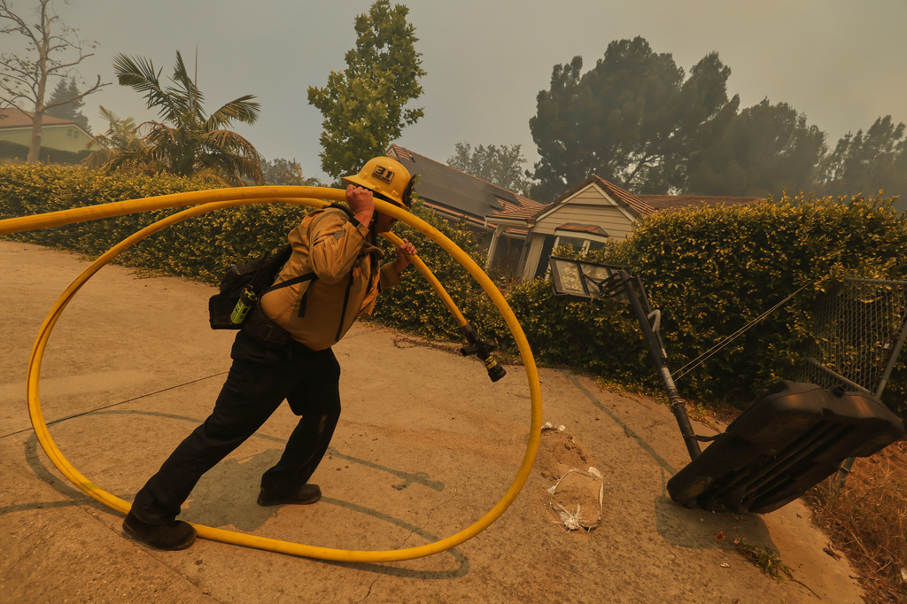 A firefighter sets up hoses while battling the Sandy Fire Monday, May 18, 2026, in Simi Valley, Calif. (AP Photo/Ethan Swope)
