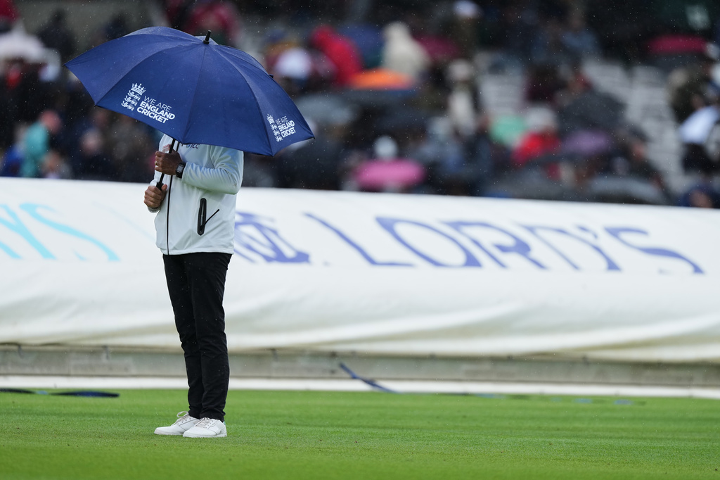An umpire stands on the field under an umbrella as it rains during the third day of the Test match between England and New Zealand at Lord's cricket ground in London, Saturday, June 6, 2026. (AP Photo/Kirsty Wigglesworth)