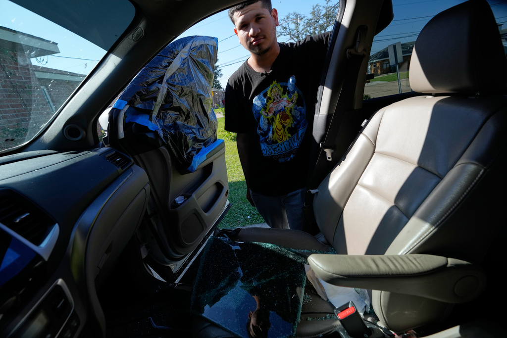 Jonathan Escalante stands over the broken window of his mother's car, which was shattered by federal immigration agents who took her away, during a federal immigration crackdown in Kenner, La., Tuesday, Dec. 9, 2025. (AP Photo/Gerald Herbert)