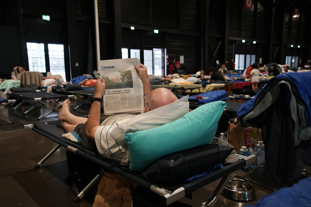 An evacuee reads a newspaper report about wildfires in southwest France as he lays on a camp bed at a temporary shelter in Bordeaux, France, Tuesday, July 28, 2026. (AP Photo/Eva van Dam)