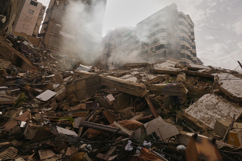 A man stands atop the rubble of a building destroyed in an Israeli airstrike as a bulldozer clears debris in Dahiyeh, Beirut's southern suburbs, Lebanon, Saturday, March 14, 2026. (AP Photo/Hassan Ammar)