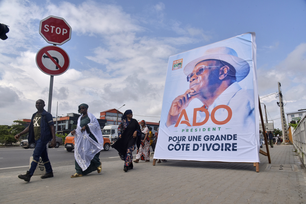 People walk past a campaign poster of President Alassane Ouattara in Abidjan, Ivory Coast, Friday, Oct. 10, 2025 (AP Photo/Diomande Ble Blonde)