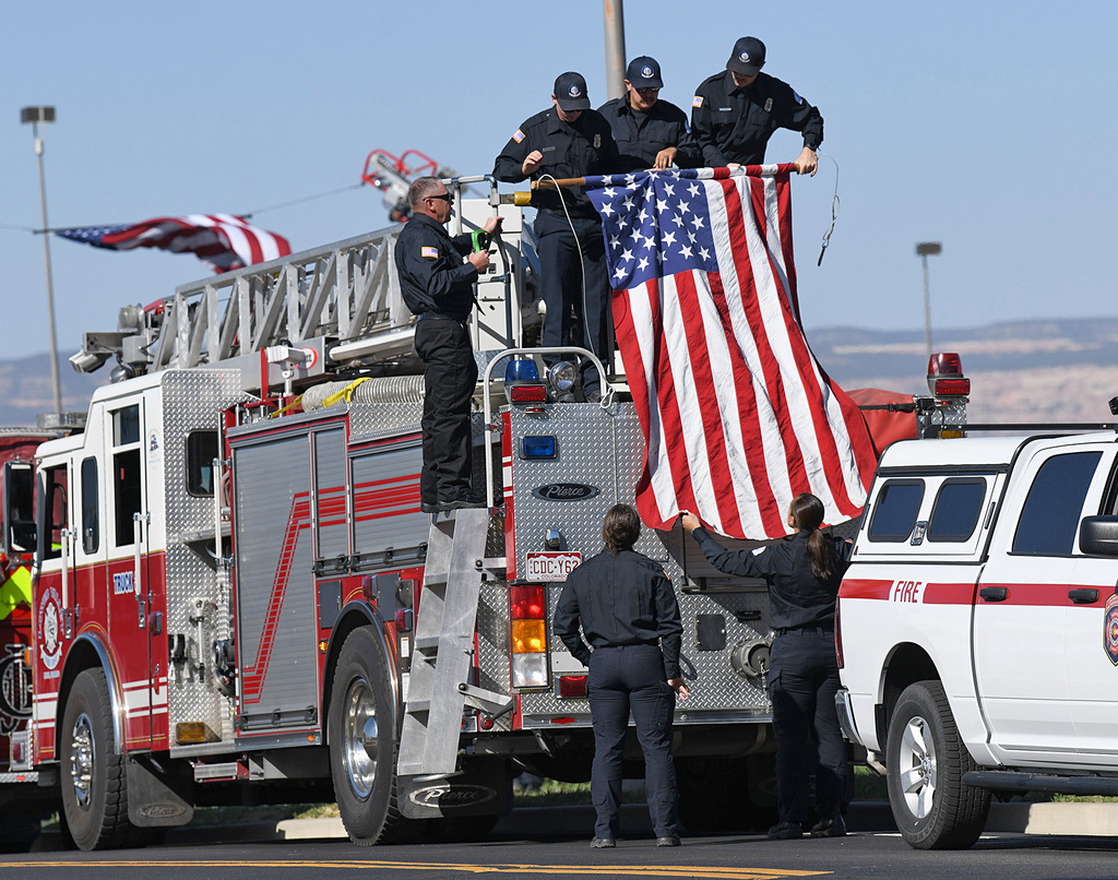 Firefighters with the Lower Valley Fire Protection District hang an American flag along a procession route in honor of three firefighters killed while fighting the Snyder Fire in Grand Junction, Colo. Sunday, June 28, 2026. (Gretel Daugherty via AP)