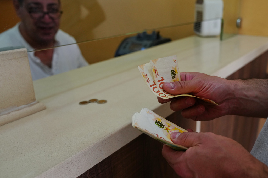 A customer counts Israeli Shekels at a currency exchange bureau in the West Bank city of Bethlehem, Tuesday, July 7, 2026. (AP Photo/Mahmoud Illean)