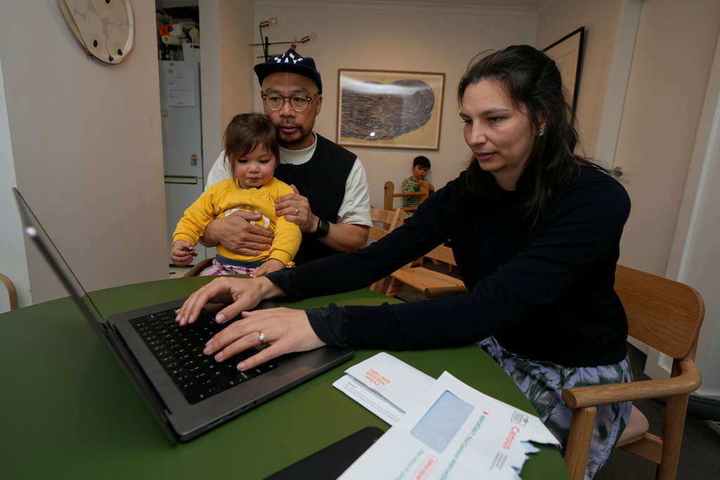 Alex Lam, right, logs onto the census website as her husband Sam, second left, holds their daughter Elodie while their son Tobi plays behind them, in Sydney, Sunday, Aug. 9, 2026. (AP Photo/Rick Rycroft)