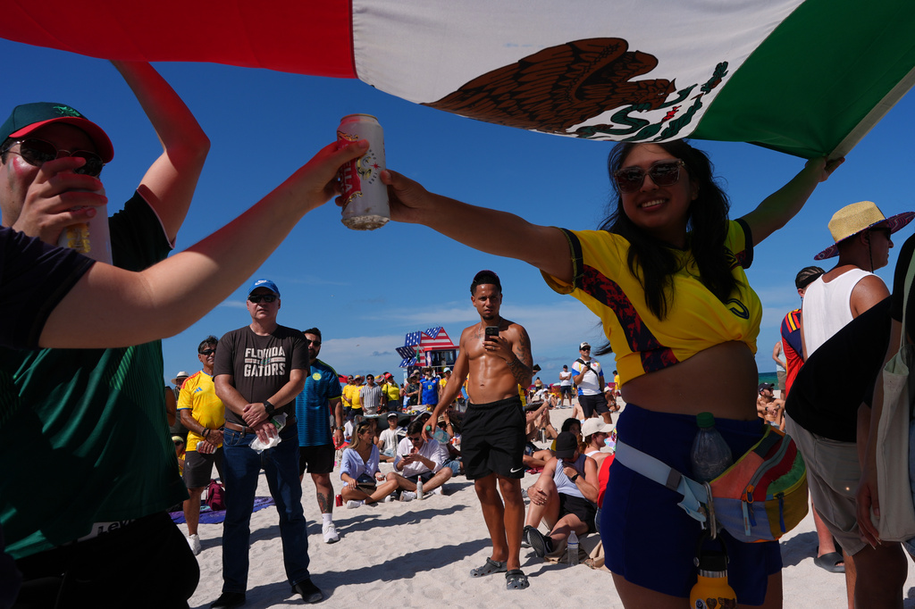 A group of fans use a Mexican flag for shade as they watch the opening World Cup Group A soccer match between Mexico and South Africa on beachfront big screens, in Miami Beach, Fla., Thursday, June 11, 2026. AP Photo/Rebecca Blackwell)