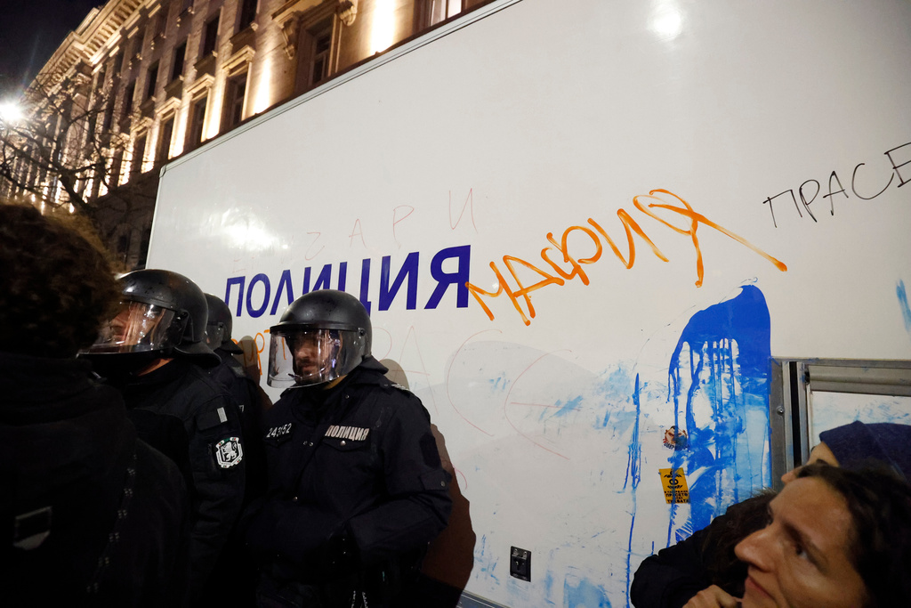 Policeman stand near a vandalized police vehicle with a graffiti sign "mafia," as thousands took to the streets of Bulgaria's capital, Sofia, to denounce steep tax hikes in next year's draft budget before being finally voted on in parliament, Wednesday, Nov 26, 2025. (AP Photo/Valentina Petrova)