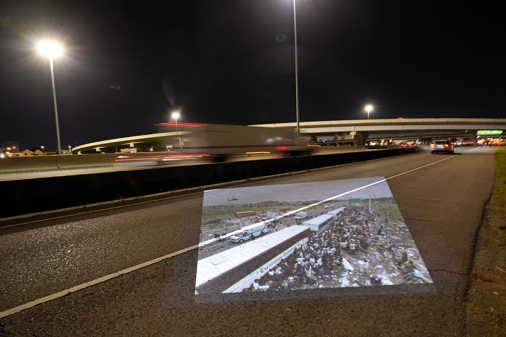 This photo showing throngs of New Orleans residents gathering at a evacuation staging area along Interstate 10 in Metairie, La., in the aftermath of Hurricane Katrina, taken by AP photographer Dave Martin, is projected Wednesday, Aug. 20, 2025, onto the same roadway. (AP Photo/Gerald Herbert)