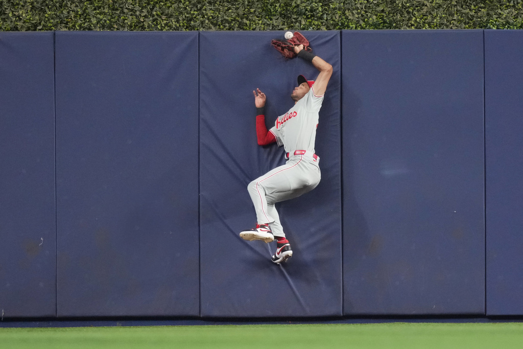 Philadelphia Phillies center fielder Justin Crawford (2) collides with the fence in center field chasing a fly ball hit by Miami Marlins shortstop Otto Lopez (6) that was later ruled a ground rule double during the first inning of a baseball game, Friday, May 1, 2026, in Miami. (AP Photo/Jim Rassol)