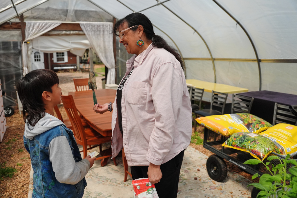 Dawn Spears, center, reacts after finding a small trowel that her grandson, Giizhig, 9, left, was looking for as they prepare tomato plants Tuesday, April 21, 2026, at a farm in Hopkinton, R.I. (AP Photo/Joshua A. Bickel)