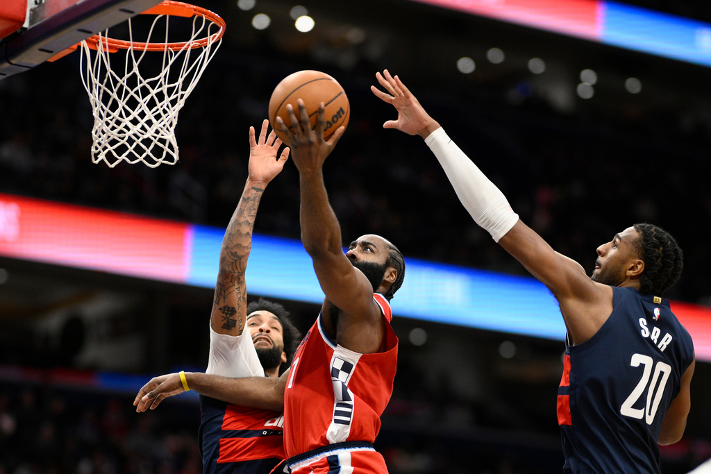 Los Angeles Clippers guard James Harden, center, goes to the basket against Washington Wizards forward Justin Champagnie, left, and center Alex Sarr (20) during the first half of an NBA basketball game, Monday, Jan. 19, 2026, in Washington. (AP Photo/Nick Wass)