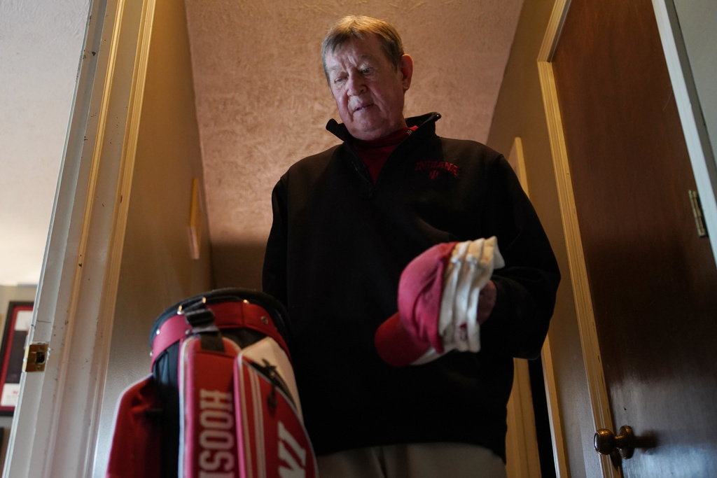 Bill Murphy, 77, an Indiana football fan, walks through the hallway of his home in Greenfield, Ind., carrying sports hats and a golf bag Wednesday Dec. 17, 2025. (AP Photo/Obed Lamy)