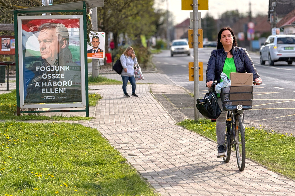 A woman rides a bicycle by an electoral poster showing Hungarian Prime Minister Viktor Orban and the slogan "Let's stand together against the war!" in Albertirsa, Hungary, Thursday, April 9, 2026. (AP Photo/Eldar Emric)