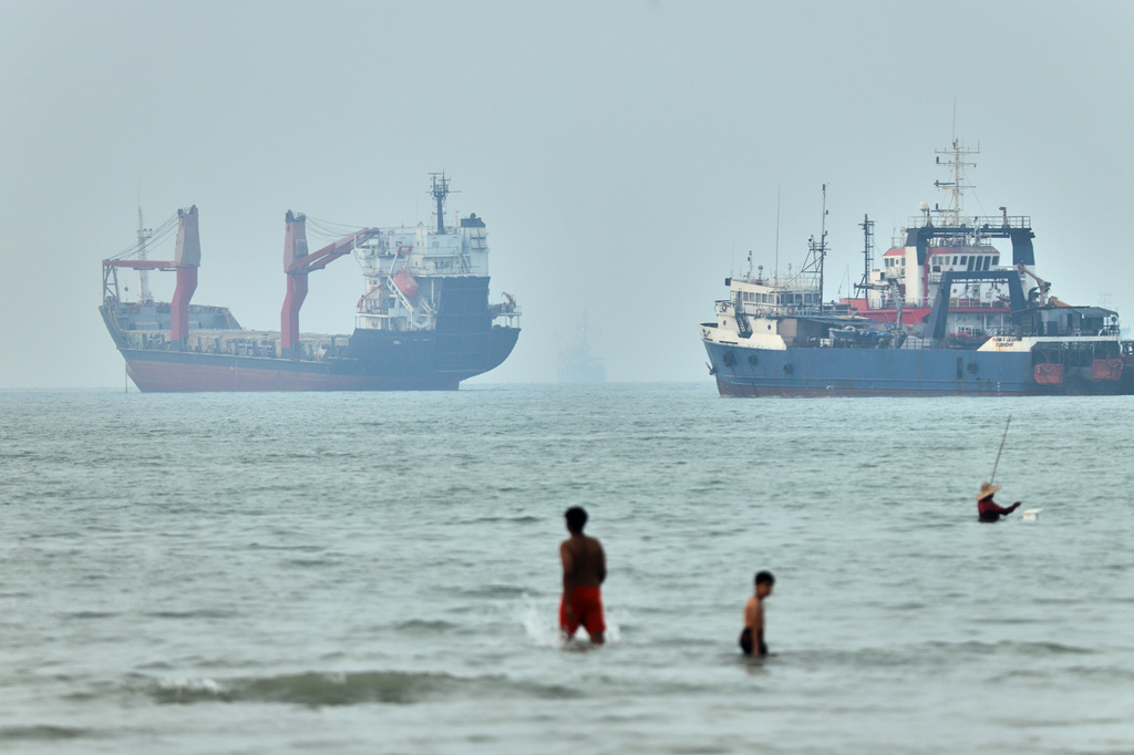 Children wade in the water with cargo ships at anchor in the background and a fisherman nearby, in the Strait of Hormuz off Bandar Abbas, Iran, Tuesday, June 30, 2026. (Amirhosein Khorgooi/ISNA via AP)