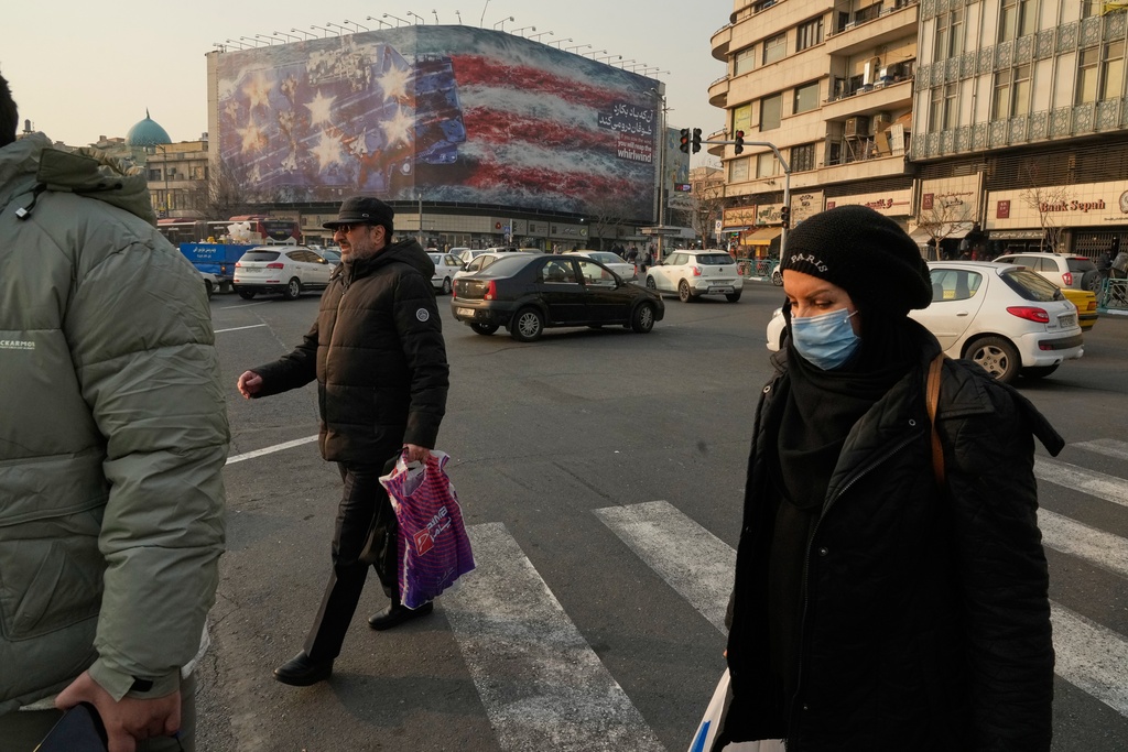 People walk past a billboard depicting a damaged U.S. aircraft carrier with disabled fighter jets on its deck and a sign reading in Farsi and English, "If you sow the wind, you'll reap the whirlwind," at Enqelab-e-Eslami (Islamic Revolution) Square in Tehran, Iran, Sunday, Jan. 25, 2026. (AP Photo/Vahid Salemi)
