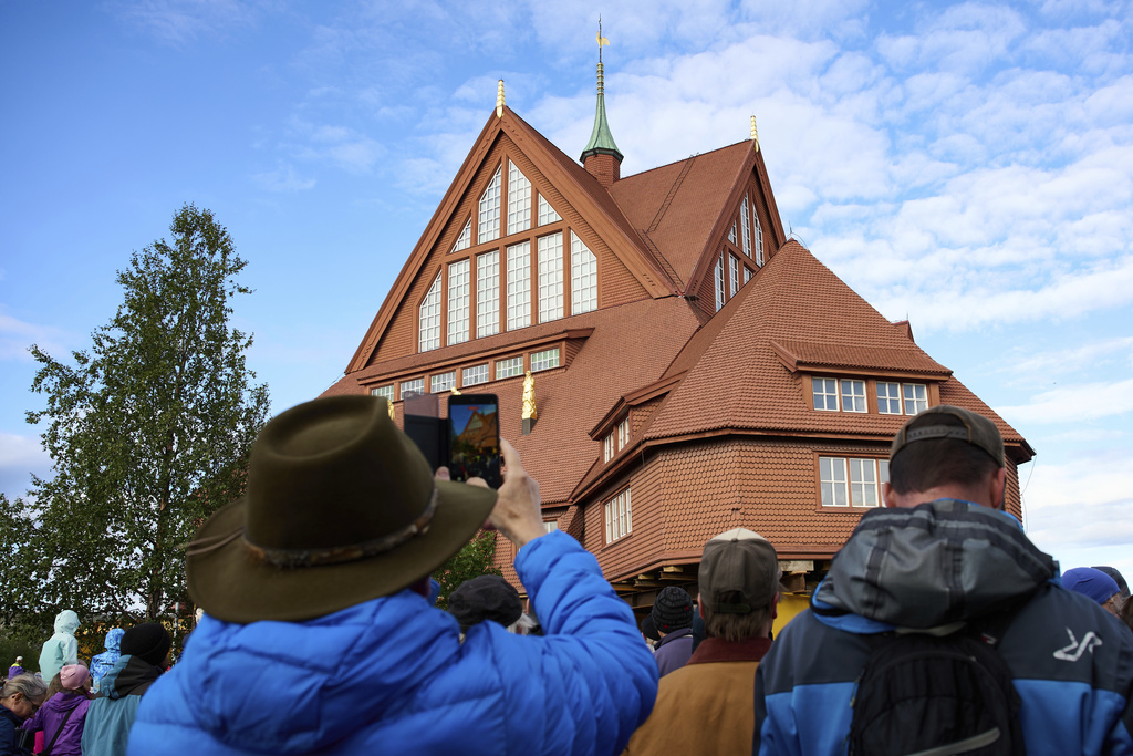 People take photographs outside the Kiruna Church, a Sami style wooden Swedish Lutheran church, called Kiruna Kyrka in Swedish, in Kiruna, Sweden, Tuesday, Aug. 19, 2025, as it is being moved along a 5-kilometer (3-mile) route east to a new city center as part of the town's relocation. (AP Photo/Malin Haarala)