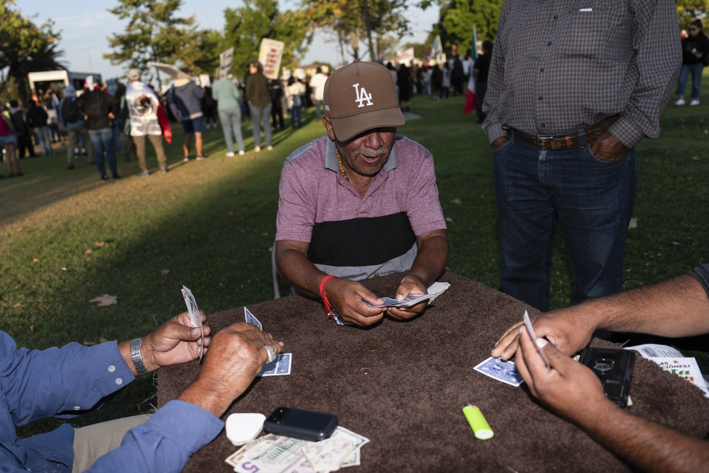 Guillermo Trejo, center, plays cards with friends at a park in Oxnard, Calif., Friday, July 18, 2025, as demonstrators gather to protest a recent ICE raid. (AP Photo/Jae C. Hong)