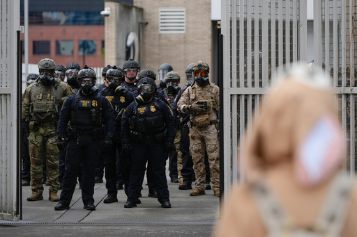 Law enforcement officers watch as the gates close at a U.S. Immigration and Customs Enforcement facility as people protest outside on Saturday, Oct. 11, 2025, in Portland, Ore. (AP Photo/Jenny Kane) Law enforcement officers watch as the gates close at a U.S. Immigration and Customs Enforcement facility as people protest outside on Saturday, Oct. 11, 2025, in Portland, Ore. (AP Photo/Jenny Kane)