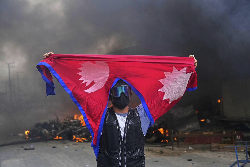 A protester shouts slogans carrying national flag after burning down a police station during protests against social media ban and corruption in Kathmandu, Nepal, Tuesday, Sept. 9, 2025. (AP Photo/Niranjan Shrestha)
