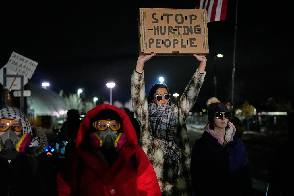 A woman holds up a sign as federal immigration officers confront protesters outside Bishop Henry Whipple Federal Building, Thursday, Jan. 15, 2026, in Minneapolis. (AP Photo/Yuki Iwamura)