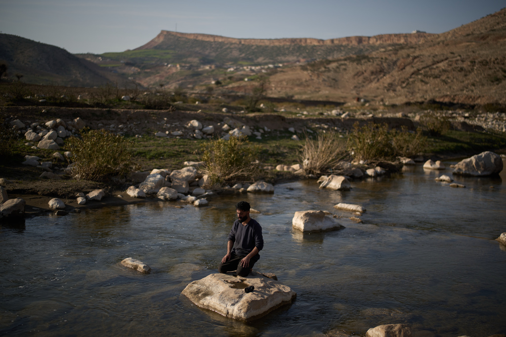 A Muslim worker prays while kneeling on a rock in a river bed as he breaks from his work at a traditional charcoal production site in Sarkand, Iraq, Thursday, March 12, 2026. (AP Photo/Leo Correa)