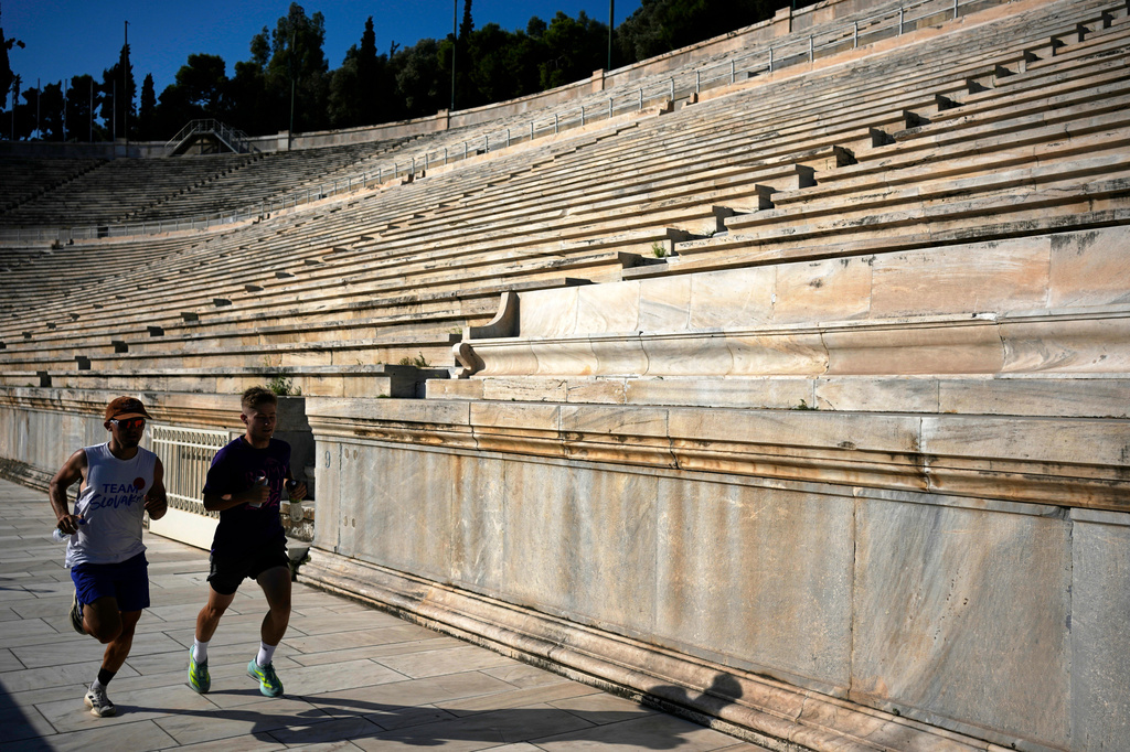 Two men run at the Panathenaic Stadium, also known as "Kallimarmaro," or beautiful marble, which hosted the first modern Olympic Games in 1896, during renovation work in Athens, Greece, Thursday, Aug. 13, 2026. (AP Photo/Thanassis Stavrakis)