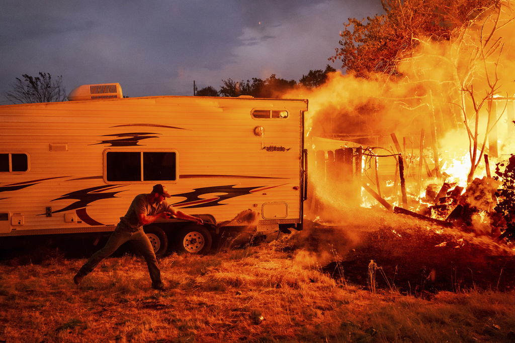 A resident works to stop flames from a burning home from spreading to a neighboring house as the 6-5 Fire burns through the Chinese Camp community of Tuolumne County, Calif., on Tuesday, Sept. 2, 2025. (AP Photo/Noah Berger)