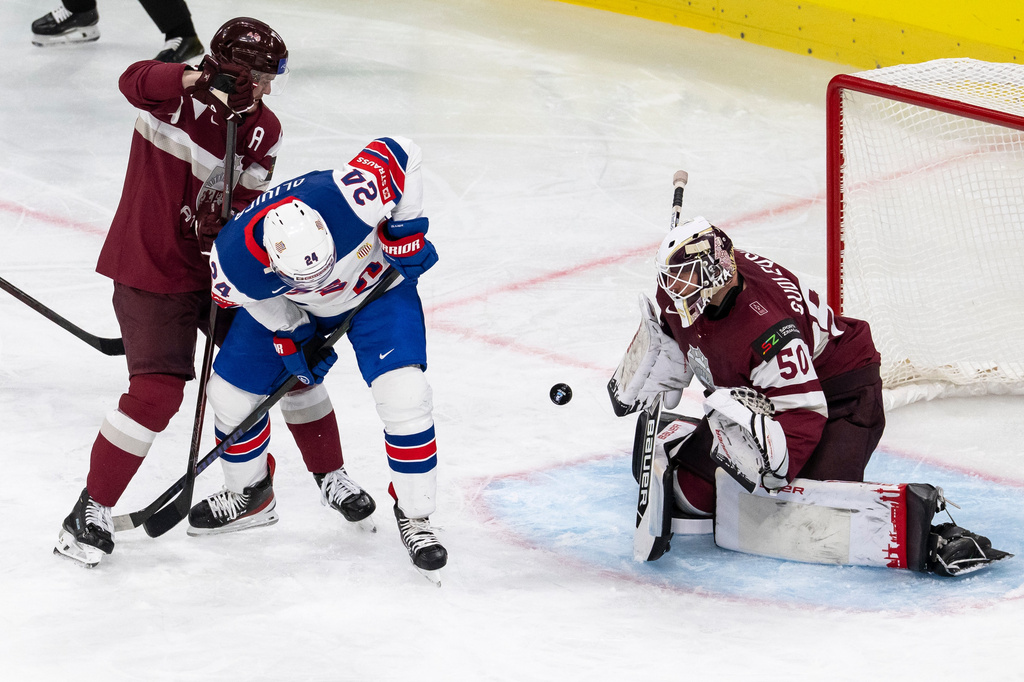 From left, Latvia's Kristaps Zile, USA's Mathieu Olivier and Latvia's goaltender Kristers Gudlevskis challenge for the puck during the 2026 IIHF Men's Ice Hockey World Championship preliminary round group A match between Latvia and the United States in Zurich, Switzerland, Saturday, May 23, 2026. (Andreas Becker/Keystone via AP)