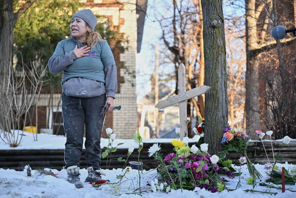 A protester stands next to a makeshift memorial honoring the victim of a fatal shooting involving federal law enforcement agents, near the scene in Minneapolis, Wednesday, Jan. 7, 2026. (AP Photo/Tom Baker)