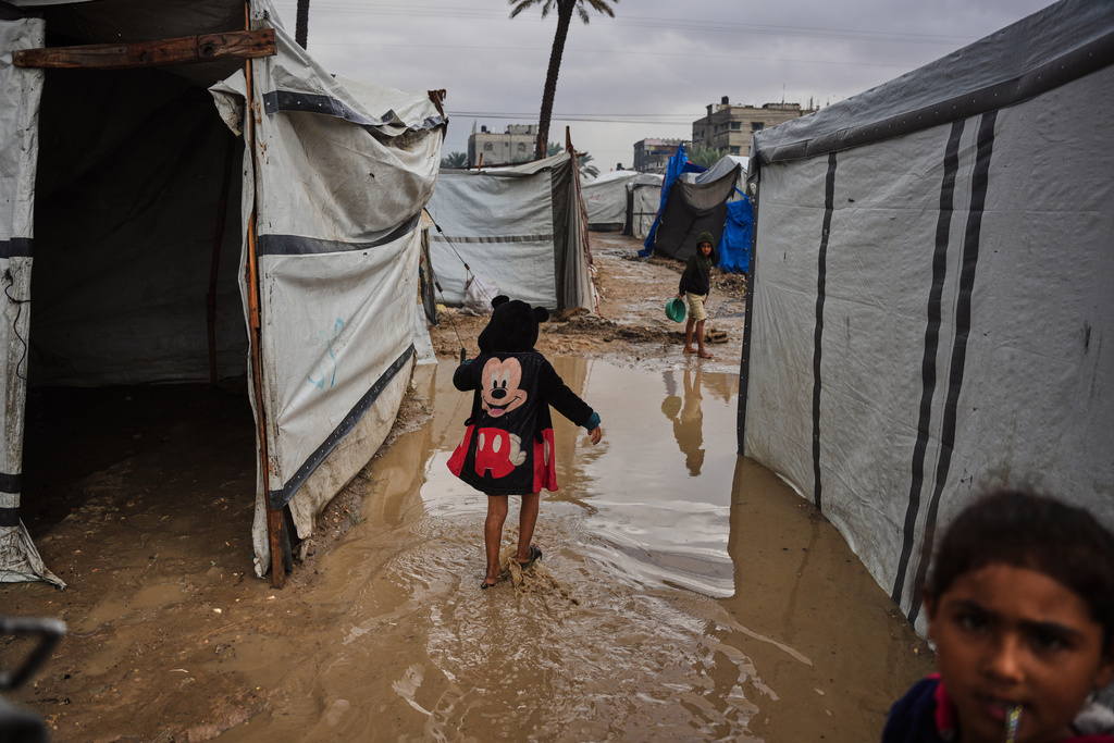 Palestinians walk through a flooded temporary tent camp after heavy rainfall in Deir al-Balah, central Gaza Strip, Tuesday, Nov. 25, 2025. (AP Photo/Abdel Kareem Hana)