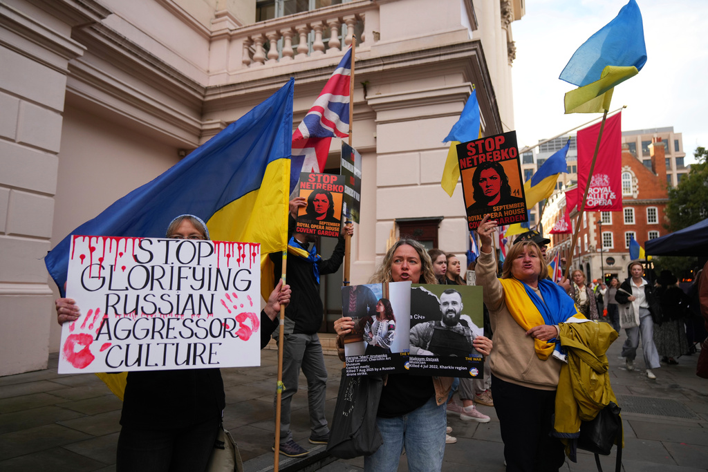 Pro-Ukraine protesters hold up placards and flags during a demonstration against the Royal Opera House in London, as the house had set an Russian opera singer to perform the lead in Puccini's Tosca. Thursday, Sept. 11, 2025. (AP Photo/Joanna Chan)
