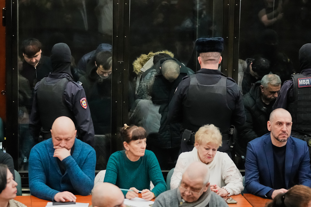 Men tried on the charges of involvement in a terror attack at the Crocus City Hall in March 2024, background, listen to the verdict from behind a glass cage at the Second Western District Military Court in Moscow, Russia, Thursday, March 12, 2026. (AP Photo/Pavel Bednyakov)