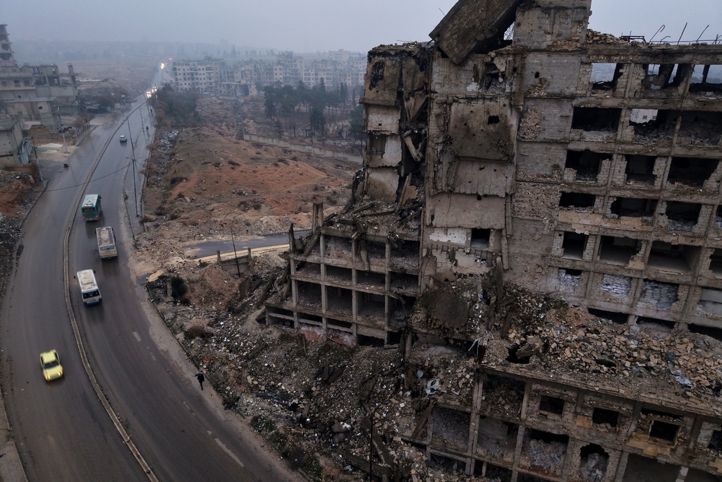 Buses carrying displaced residents drive past a building in ruins as they return to the Achrafieh neighborhood after days of fighting between government forces and Kurdish fighters in the northern city of Aleppo, Syria, Monday, Jan. 12, 2026. (AP Photo/Omar Albam)