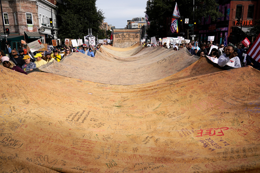Demonstrators carry a signed banner representing the U.S. Constitution as they rally at the 14th and U street corridor before marching to the national Mall during a No Kings protest in Washington, Saturday, Oct. 18, 2025. (AP Photo/Jose Luis Magana)