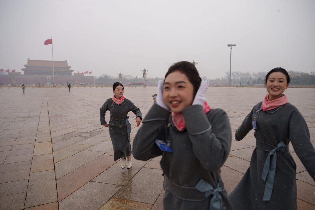 Hostesses react during a snow fall ahead of the pre session of the National People's Congress (NPC) at Tiananmen Square in Beijing, China, Wednesday, March 4, 2026. (AP Photo/Vincent Thian)