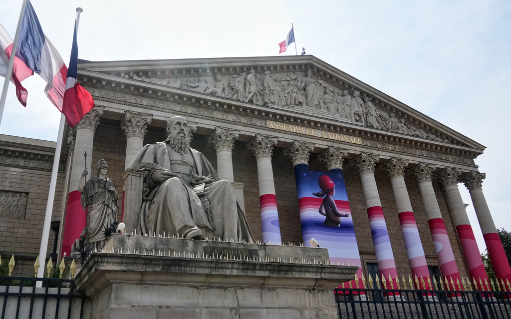 The French National Assembly is draped with the artwork "Marianne rêve" ("Marianne Dreams") by French street artist Seth, depicting Marianne the symbol of the French Republic, before lawmakers vote later on final approval of a bill allowing adults with incurable illnesses to receive lethal medication, in Paris, Wednesday, July 15, 2026. (AP Photo/Michel Euler)