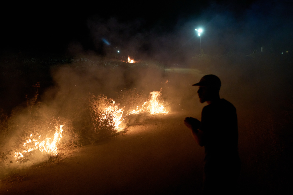 A Palestinian stands next to a fire after brush was set ablaze on the roadside to prevent an Israeli settler attack in the West Bank village of Sinjil, Friday, July 17, 2026. (AP Photo/Leo Correa)