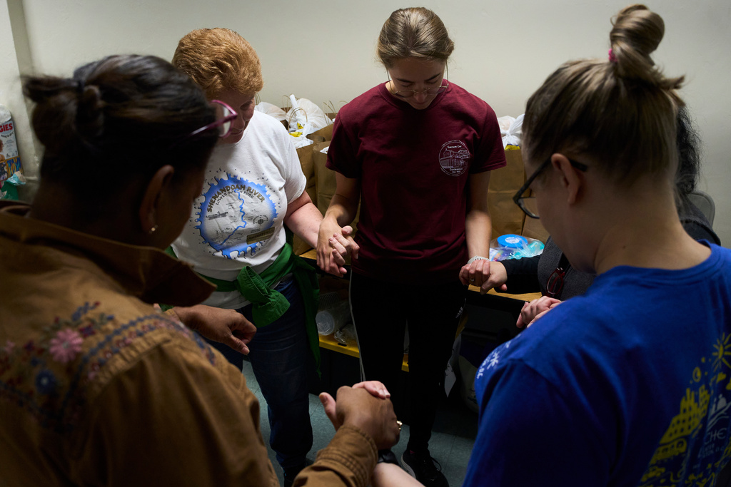 Parishioners of the Shrine of the Sacred Heart and volunteers pray in the church's basement before delivering donated food to families who are afraid to leave their homes to go to the grocery store due to immigration raids in Washington, Oct. 11, 2025. (AP Photo/Luis Andres Henao)