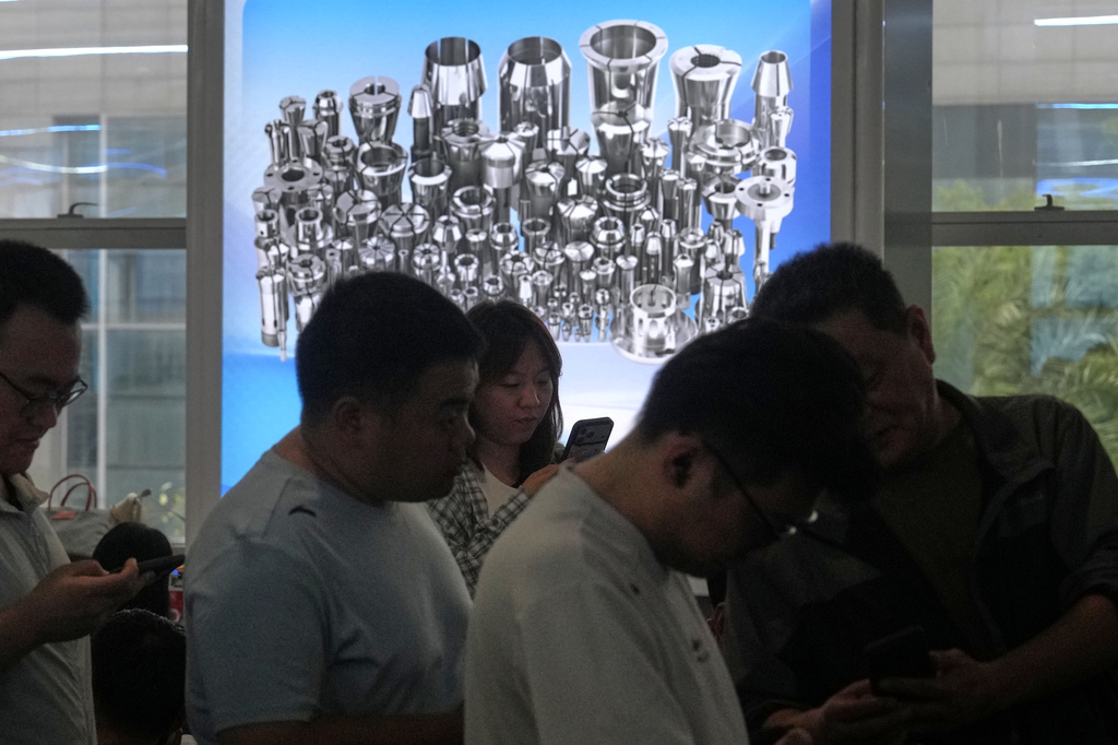 Passengers line up at a departure hall near an electronic board advertising a factory manufacturing machinery parts, at a train station in Shanghai, China, Monday, Oct. 19, 2026. (AP Photo/Andy Wong)
