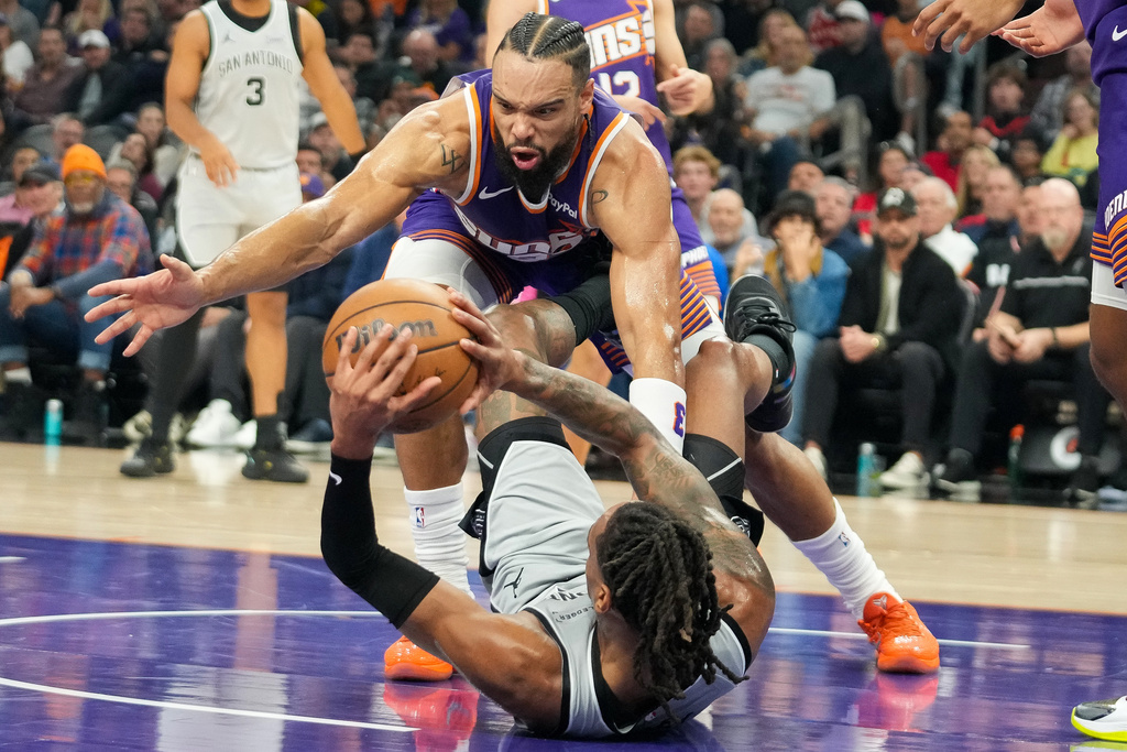 Phoenix Suns forward Dillon Brooks, top, goes for a loose ball against San Antonio Spurs guard Devin Vassell, bottom, during the first half of an NBA basketball game in Phoenix, Sunday, Nov. 23, 2025. (AP Photo/Darryl Webb)