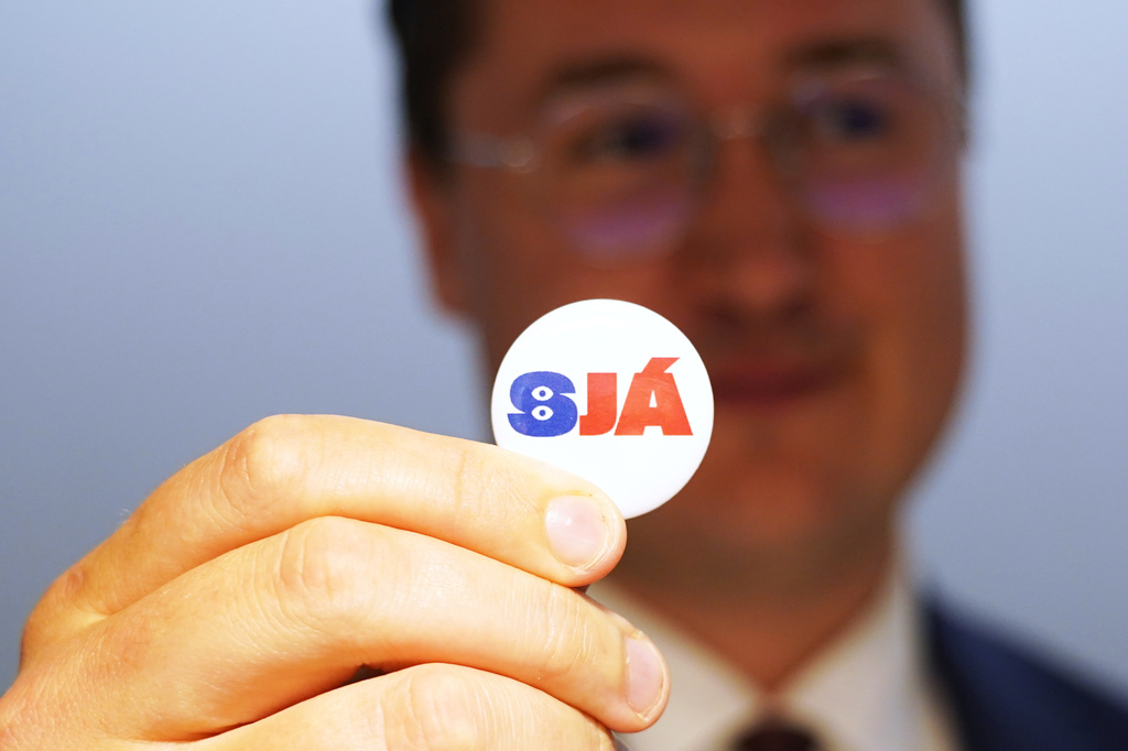 A man holds a badge reading "See", at the opening of the "Yes" campaign's office in Reykjavik, Iceland, Friday, Aug. 7, 2026. (AP Photo/James Brooks)