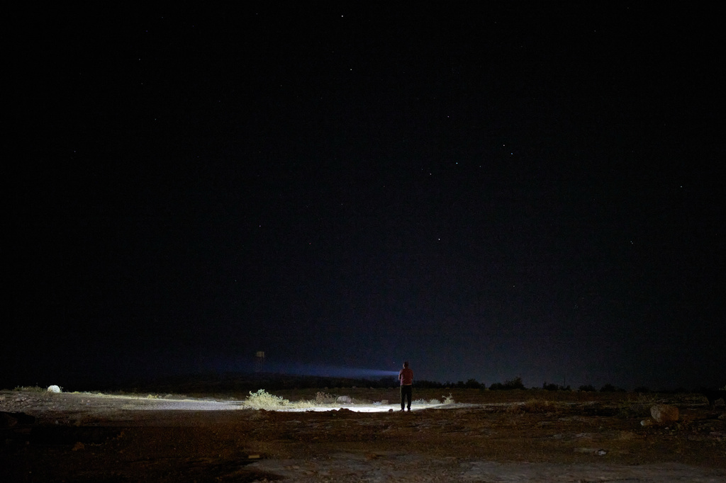 A Palestinian uses a flashlight as he takes part in a night watch to warn neighbors if Israeli settlers approach his community near the West Bank village of Susya, in the Masafer Yatta region, Thursday, June 18, 2026.. (AP Photo/Leo Correa)
