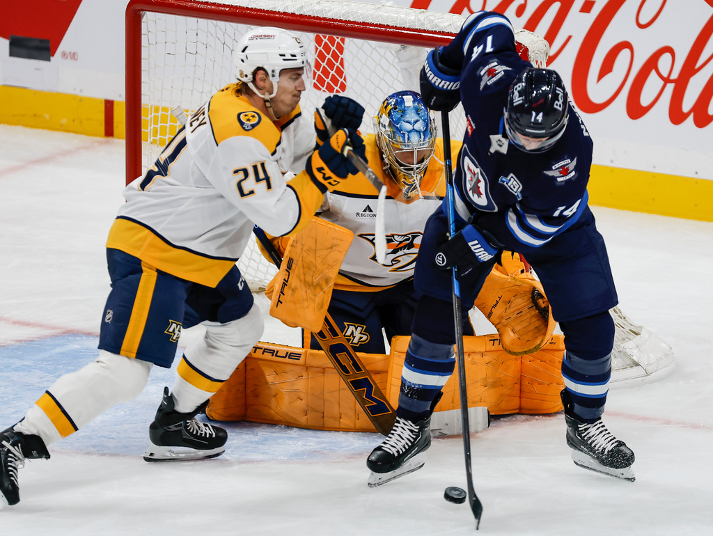 Winnipeg Jets' Gustav Nyquist (14) tries to tip the puck as Nashville Predators' Spencer Stastney (24) defends for goaltender Juuse Saros, center, during second-period NHL hockey game action in Winnipeg, Manitoba, Saturday, Oct. 18, 2025. (John Woods/The Canadian Press via AP)