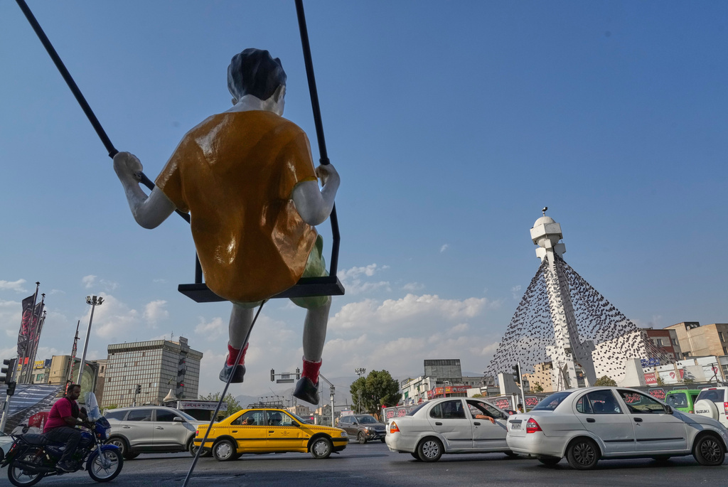 Vehicles drive past a statue of a swinging boy at a square in Tehran, Iran, Monday, Aug. 10, 2026. (AP Photo/Vahid Salemi)