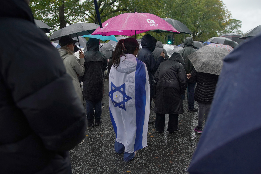 A woman wears the flag of Israel wrapped over her back as she attends a vigil for the victims of the attack on at Heaton Park Hebrew Congregation synagogue, in Crumpsall, Manchester, England, Friday, Oct. 3, 2025. (AP Photo/Ian Hodgson)
