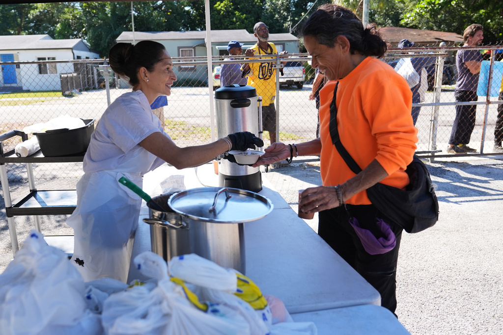 Volunteer Blanca Flores, left, passes out hot coffee, oatmeal and bags of food at a food distribution held by the Village (FREE)DGE at the Freedom Lab, Monday, Nov. 3, 2025, in Miami. (AP Photo/Lynne Sladky)
