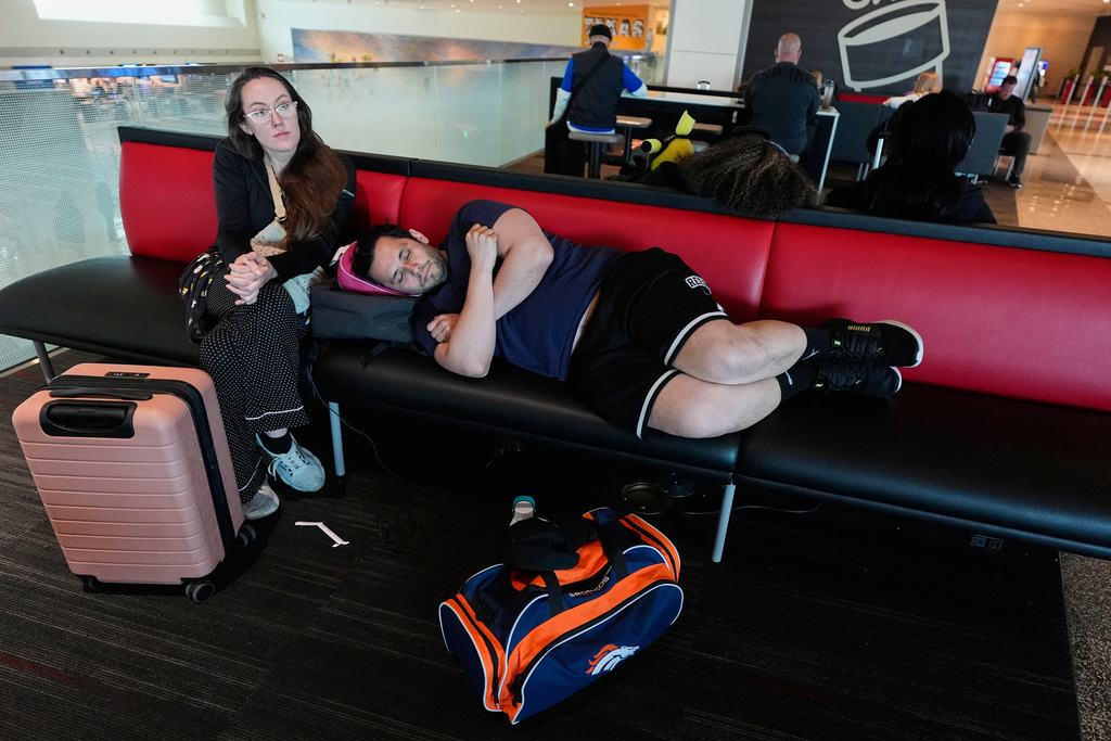 Jamie Sims left, and Carlos Serna, right, try to get some rest as they wait for their cancelled flight to El Paso, texas to be rescheduled at Love Field Airport in Dallas, Monday, March 16, 2026. (AP Photo/Tony Gutierrez)