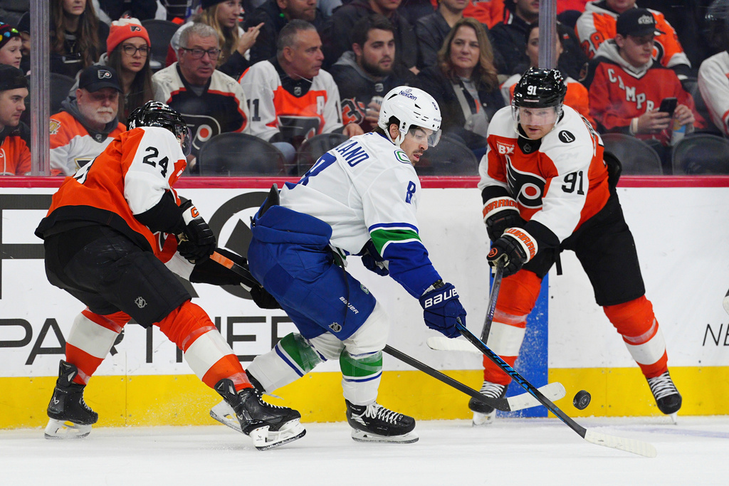 Vancouver Canucks' Conor Garland, center plays the puck past Philadelphia Flyers' Nick Seeler (24) and Carl Grundstrom (91) during the first period of an NHL hockey game, Monday, Dec. 22, 2025, in Philadelphia. (AP Photo/Derik Hamilton)