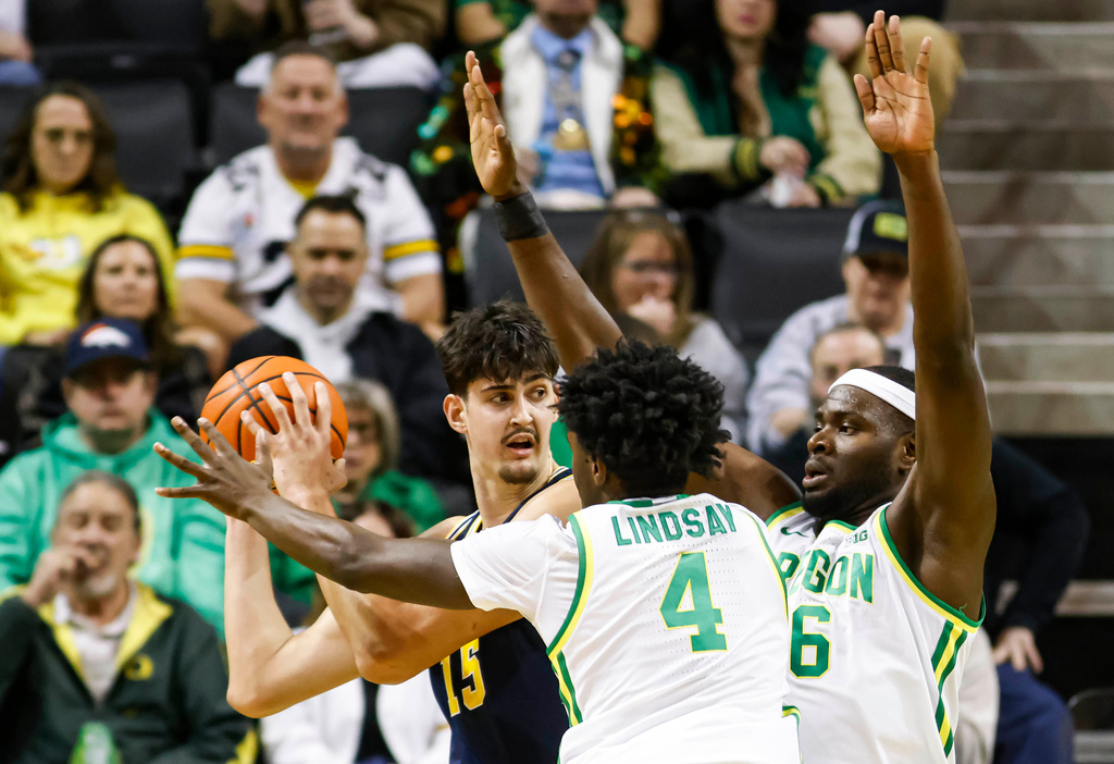 Michigan center Aday Mara (15) attempts to pass against Oregon forward Dezdrick Lindsay (4) and forward Oleksandr Kobzystyi (6) in the first half of an NCAA college basketball game in Eugene, Ore., Saturday, Jan. 17, 2026. (AP Photo/Thomas Boyd)
