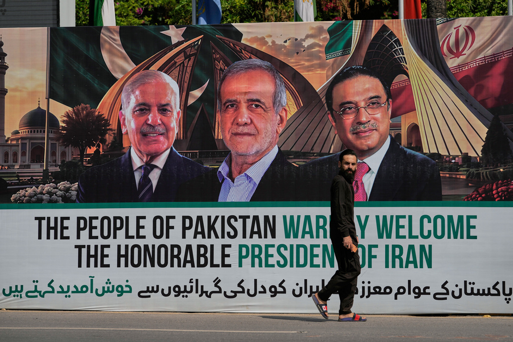 A man walks past a welcoming billboard featuring Iranian President Masoud Pezeshkian, center, with Pakistan President Asif Ali Zardari, right, and Shehbaz Sharif along a roadside in Islamabad, Pakistan, Tuesday, June 23, 2026. (AP Photo/Anjum Naveed)